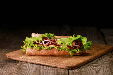 用生菜火腿奶酪培根和番茄放在木制切菜板上的新鲜三明治图片