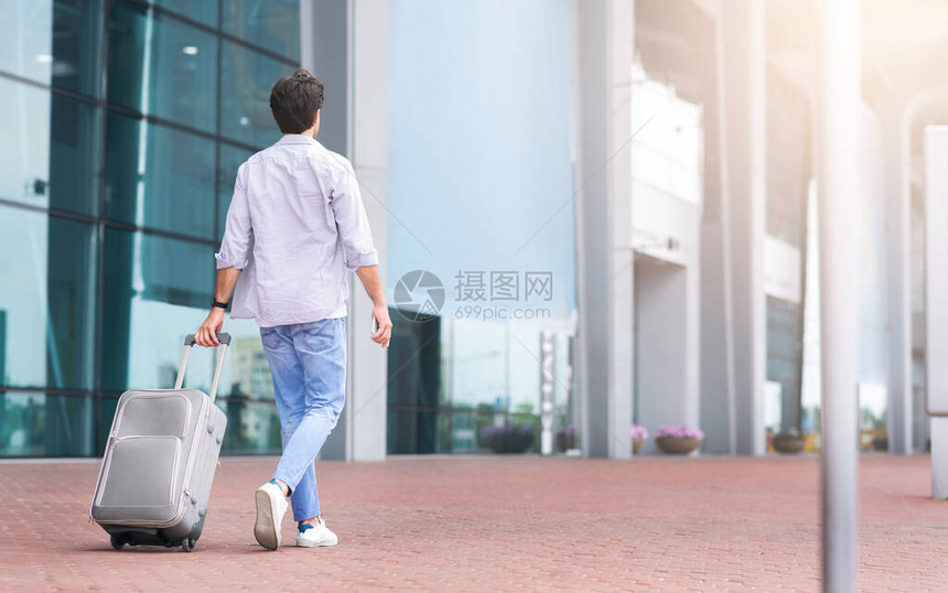 青年男子带着手提箱走出机场前往出租车点复制空间的后图片
