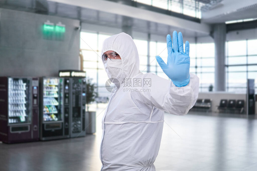 身着一次防疫抗菌隔离套装的男流行病学家在机场或火车站的候诊室中表图片