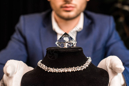 持有项链的珠宝估价员与黑底项链和宝石的珠宝展台图片