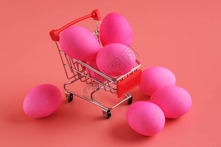 粉红色背景上的复活节彩蛋和带鸡蛋的手推车购物车复活节购物和销图片