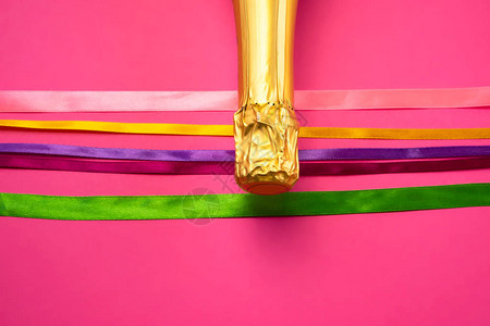 金箔香槟瓶颈和亮粉色背景上的彩色缎带图片