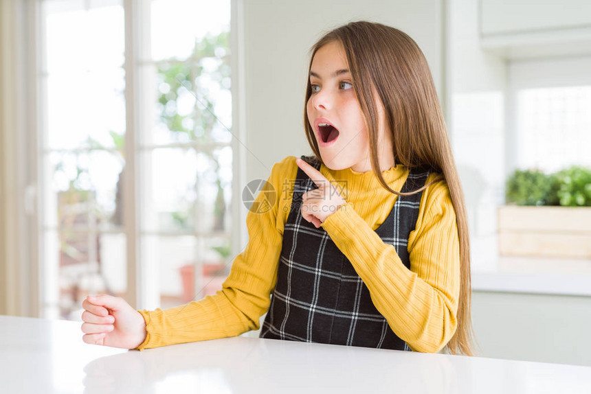 穿着黄毛衣的年轻金发女孩突然用手指对着另一边张开嘴惊讶地表露图片