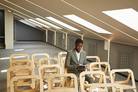 成功的非裔美籍商人坐在室内空会议室大厅复制空间的观众席上图片