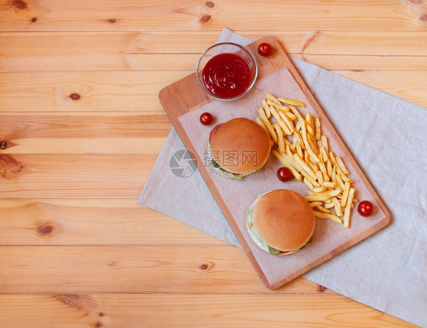 两块汉堡和两块炸土豆放在木制餐桌上的切割板上顶层视图片