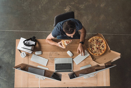 编程员在工作场所食披萨和使用计算机图片