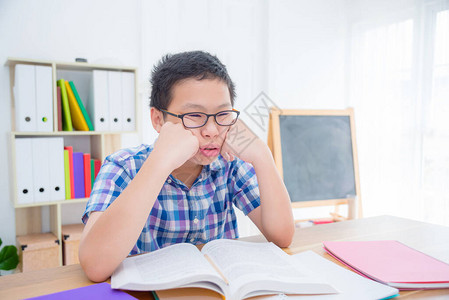 年青的亚洲男孩感到疲倦和困于阅读图片