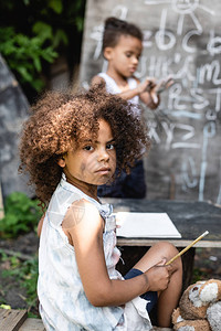 在非洲儿童坐在小孩和黑板附近时持有铅笔的非洲儿童有选择图片