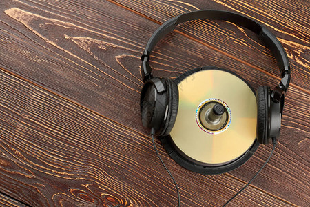 光盘和副本空间上的耳机黑色耳机与棕色木制背景上的光盘音图片