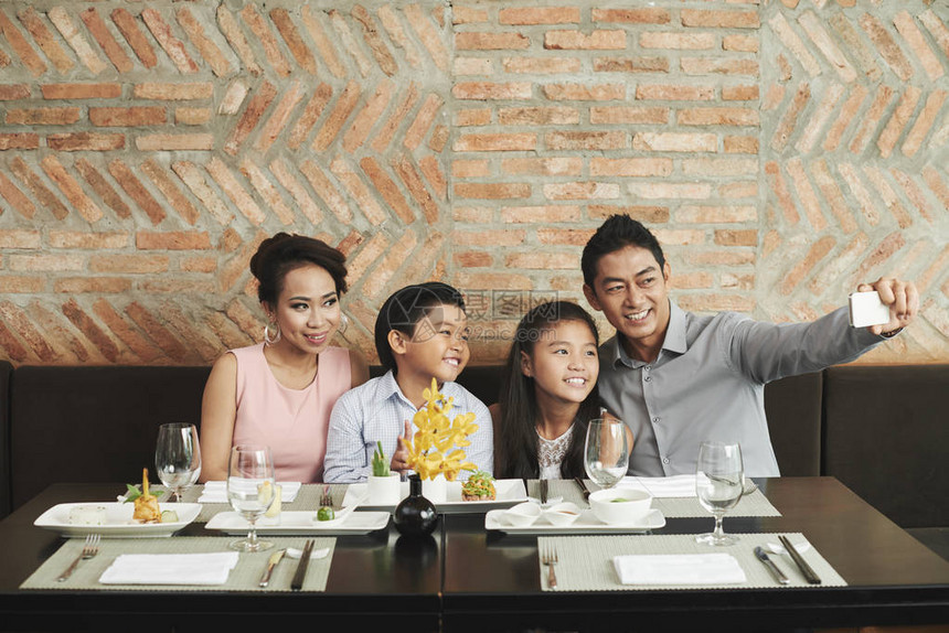 快乐的亚洲家庭在餐厅桌前拍摄自己照片并图片