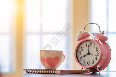 闹钟和咖啡杯放在窗边的木桌上图片