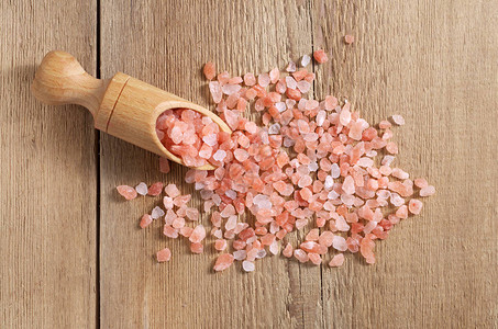 粉色盐在勺子中在木制桌子图片