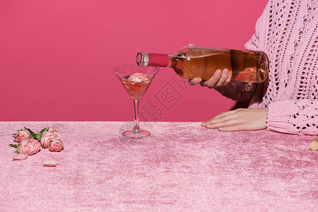 女在丝绒布上的玫瑰花瓣附近倒玫瑰酒背景