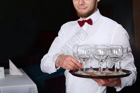 一个年轻的男服务员端着酒杯放在托盘上餐厅内部没有人脸的照片餐饮图片