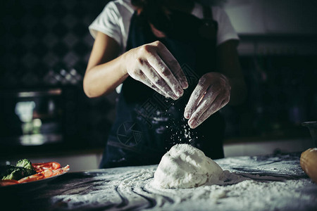 妇女在准备做比萨饼时把面粉倒在面团图片