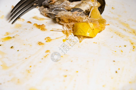 晚餐剩下的剩菜放在肮脏的白色盘子鱼骨头和柠檬片上背景图片