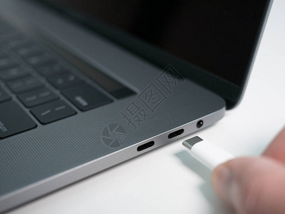 将白色USBCTypeC或Thunderbolt3电缆手动插入灰色笔记本电脑笔记本背景图片