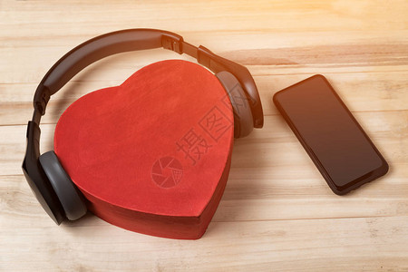 全尺寸无线耳机停在红心形盒子和浅棕色木制桌子上图片