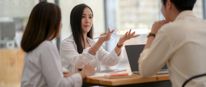 年轻大学生在木制桌子上用数字设备做介绍时举行小组简报的裁剪图片