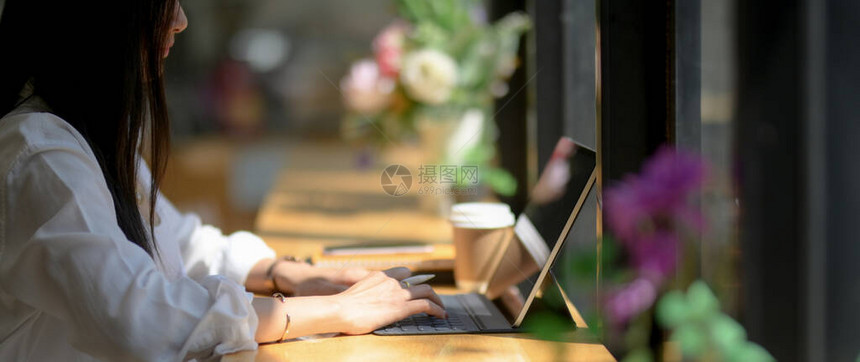 年轻女大学生在咖啡店的木制柜台上用数字平板电脑专注于她图片