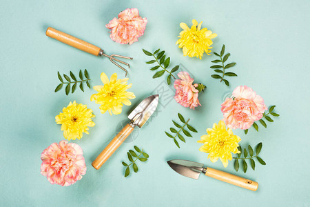 花园手工具绿帆布背景上的粉花和黄花图片