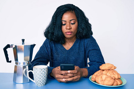 用智能手机的思维态度和冷静的表情吃早餐的美丽非洲女人图片