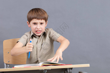 一个小学生正在做作业课桌旁拿着课本的孩子很生气男孩不想学习一个七岁的图片
