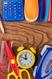 木制背景的学校或办公室用品闹钟计算器和各种文具物品文图片