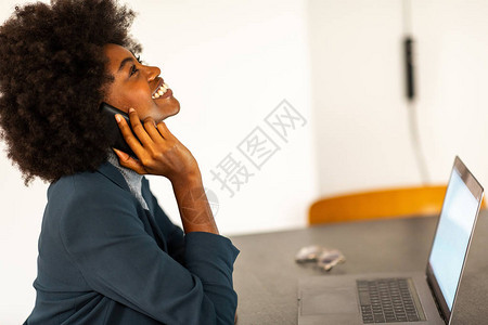 坐在办公室用手机和笔记本电脑工作的非洲女商人的侧面肖像背景图片