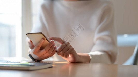 坐在简单工作场所时使用智能手机的年轻女大学图片