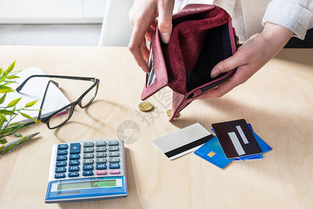 妇女手拿空钱包几枚硬币和信用卡与计算器放在桌面上失业和解雇概念货币危图片