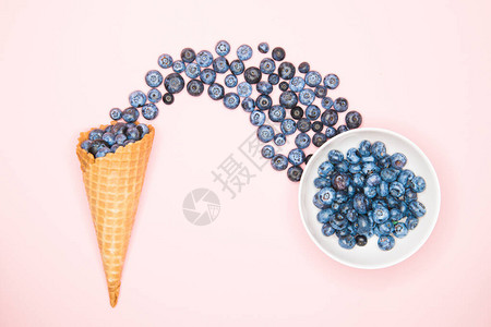 粉红色背景上的冰淇淋蛋筒中的新鲜蓝莓蓝莓爆炸暑假概念平躺图片