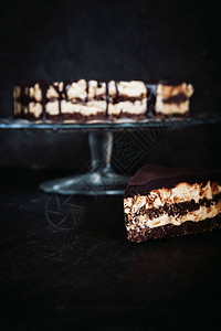 切片和巧克力蛋糕层与黄油奶坚果奶油和巧克力滴在深色木质背景的玻璃架上图片