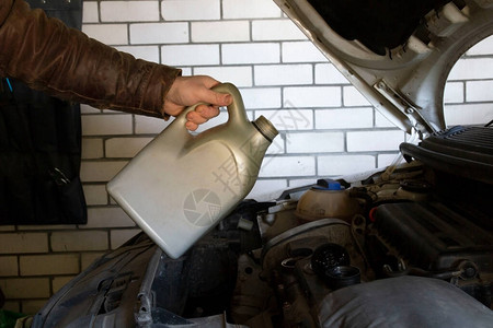 男人开始用合成马达油从塑料罐子上倒发动机油在汽车上进行修理图片