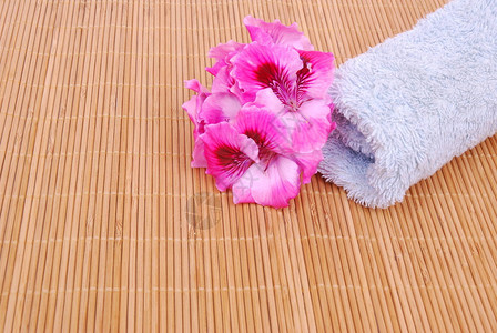 一个滚动的新鲜浴巾和美丽的粉红色花朵在竹垫图片