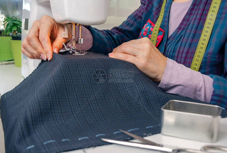 在缝纫机上处理服装的女裁缝手的特写图片