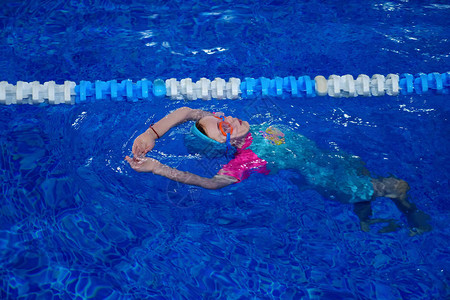 戴着护目镜泳装和帽子的小女孩正在游泳池里训练游泳图片