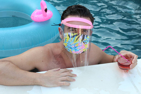 穿着医疗保护面罩的英俊青年男子在科罗纳封闭期间在游泳池里拍图片