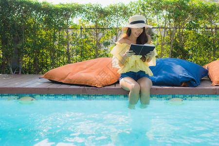 在酒店度假胜地户外游泳池周围阅读书的图片