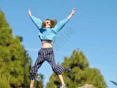一个穿着蓝色毛衣和深蓝色条纹裤的年轻女子在空中跳跃图片