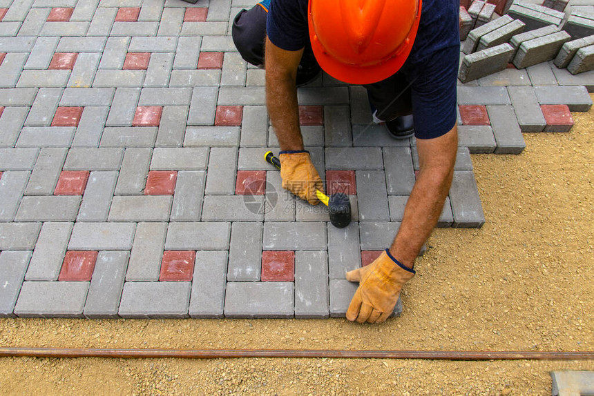 专业砌砖工在铺有衬里的沙子的基础上为道路人行道或天井安装新的瓷砖或平板在房子的院子里铺设灰色图片