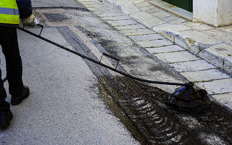 柏油路的部分修理工人在沥青表面喷洒沥青道路维护工人将沥青混合物图片