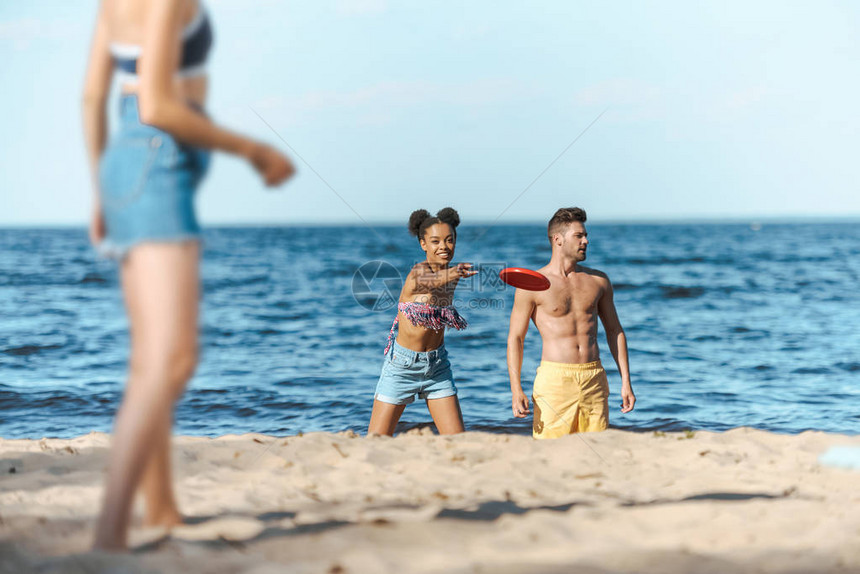 在沙滩上玩飞盘的种族间朋友有选择地聚焦于沙滩图片
