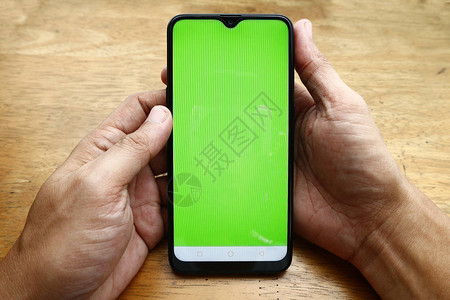 照片显示手持智能手机绿色屏幕和木制桌图片