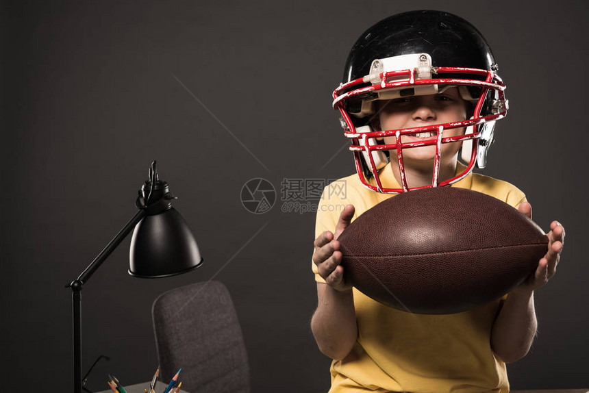 美国足球头盔中快乐的小男孩带着灰色的球图片