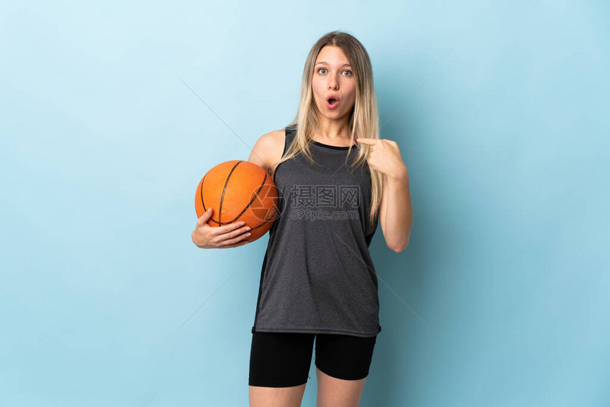 年轻金发女子打篮球孤立在蓝背景的蓝脸部图片