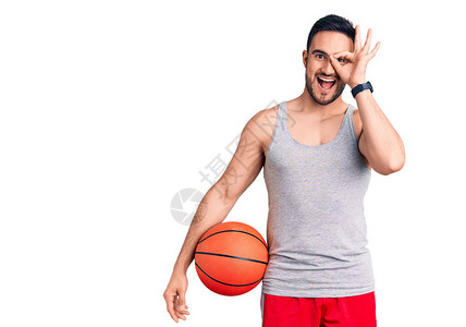 年轻英俊男人拿着篮球笑着开心地微笑着做一个好标记用手图片