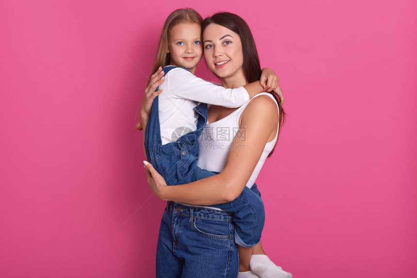 年轻迷人的母亲带着她的小女儿在粉红色的背景下拥抱和微笑图片