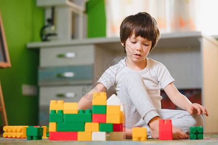 孩子们在儿童房的地板上与玩具设计师玩耍男孩玩五颜六色的积木幼图片
