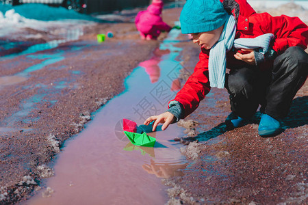 儿童在春季水坑中玩纸船儿背景
